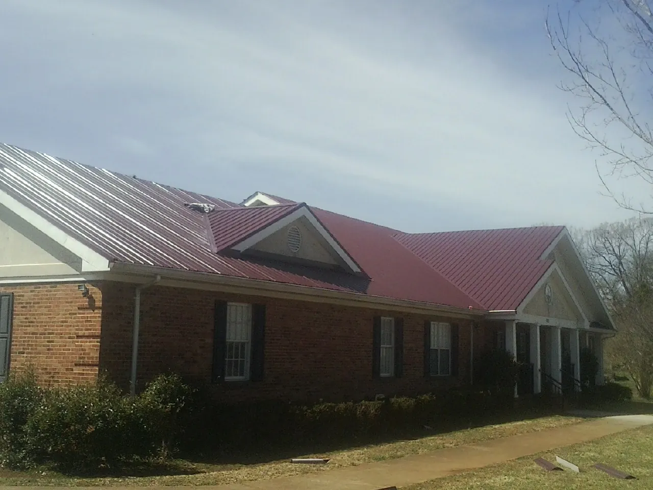 Red metal roof with gabled entries on a long brick building, from a Hail Damage Roof Repair job in South Bend